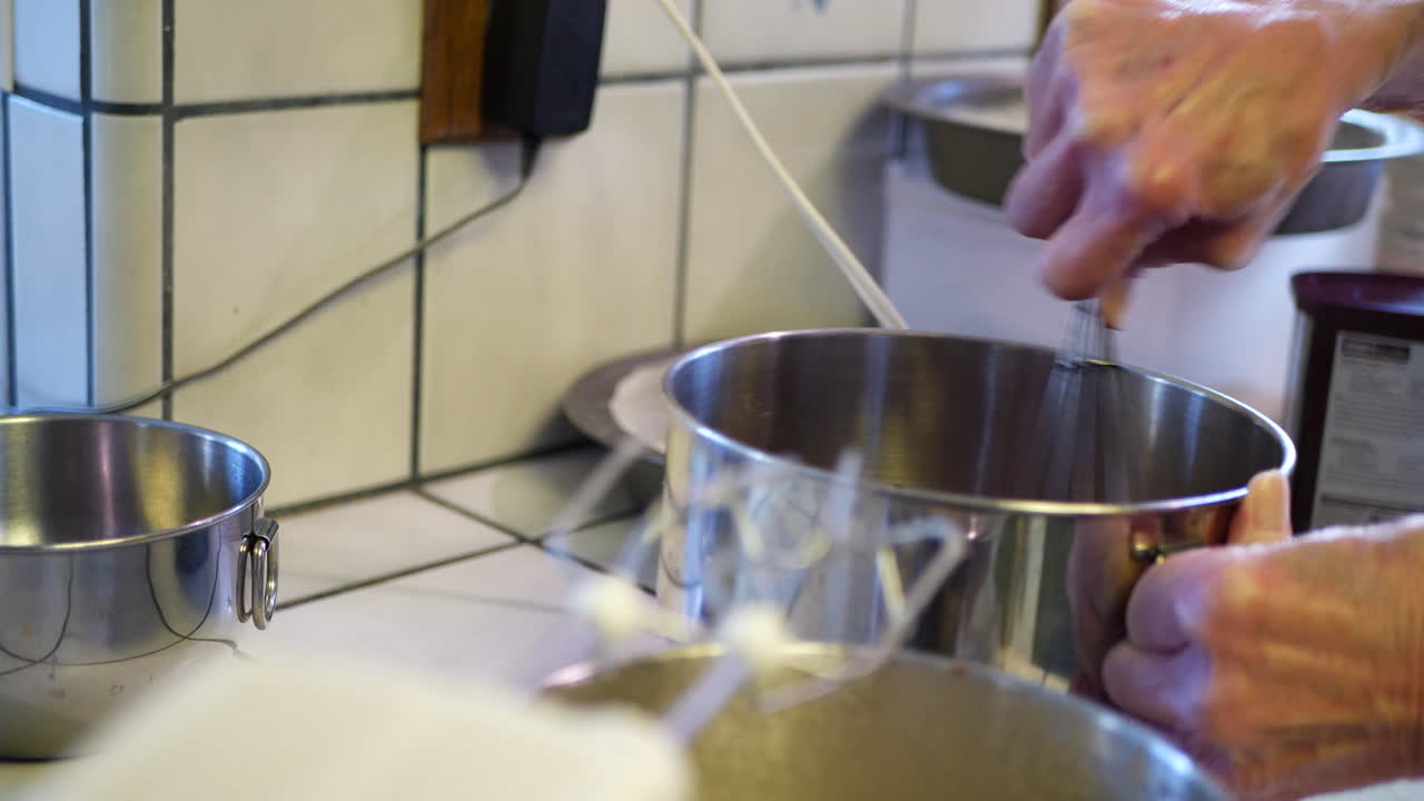 Una chef donna che usa una frusta di metallo in una ciotola per preparare una deliziosa pastella vegana per torta al cioccolato, mentre cucina un dessert in una cucina.
