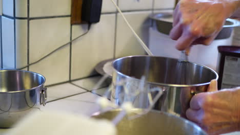 a woman chef using a metal whisk in a mixing bowl to make delicious vegan chocolate cake batter while baking dessert in a kitchen