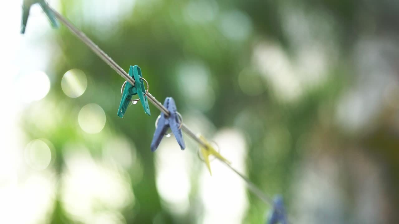 Colorful clothespins attached to a rope with water droplets. Static shot