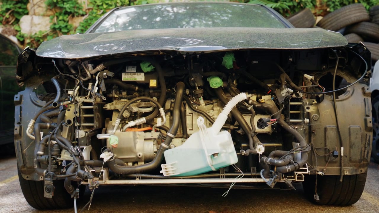 Close up front view of a dismantled car with exposed engine components, hoses, wiring, and missing body panels