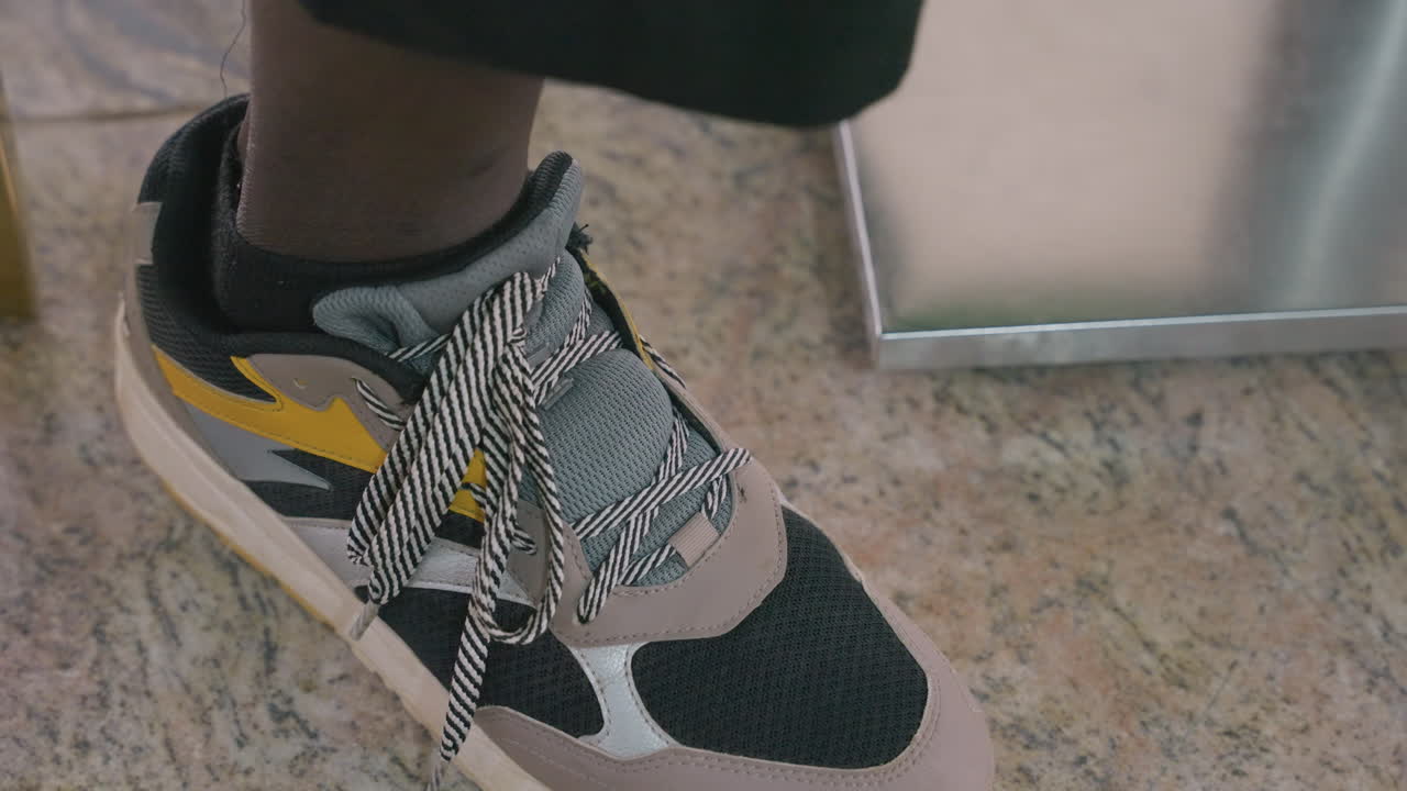 Primo piano di una sneaker sul pavimento di un caffè, scena romantica granulosa che mostra il piede e i dettagli dei lacci mentre una coppia si scambia una spinta timida sotto il tavolo vicino a una gamba di metallo del tavolo, luce calda, abbigliamento casual, momento spontaneo pieno di sottili dettagli.