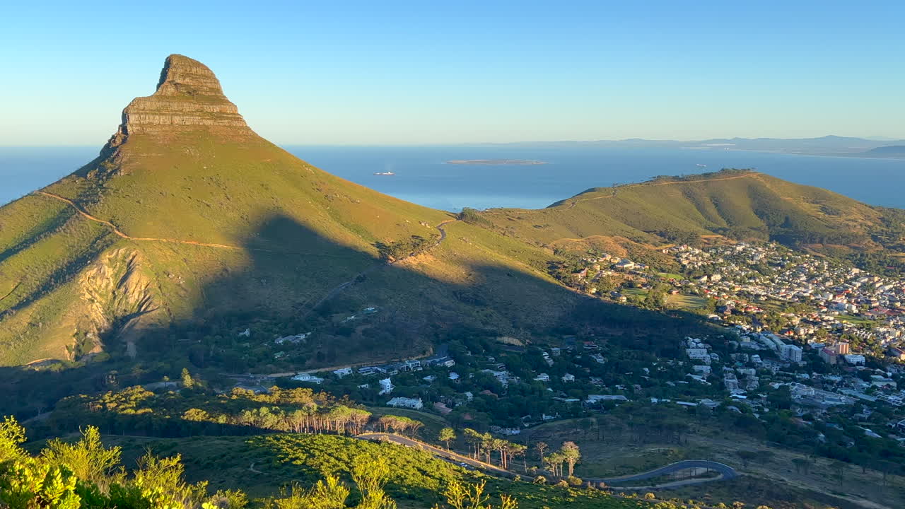 Sunrise Lion's Head morning hike exploring Table Mountain Cape Town South Africa pan right view of mountain and downtown city golden yellow sun rays lush spring summer grass and flowers deep blue sea