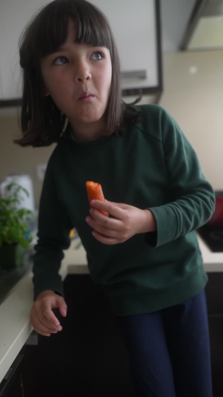 Ragazza che mangia una carota in cucina