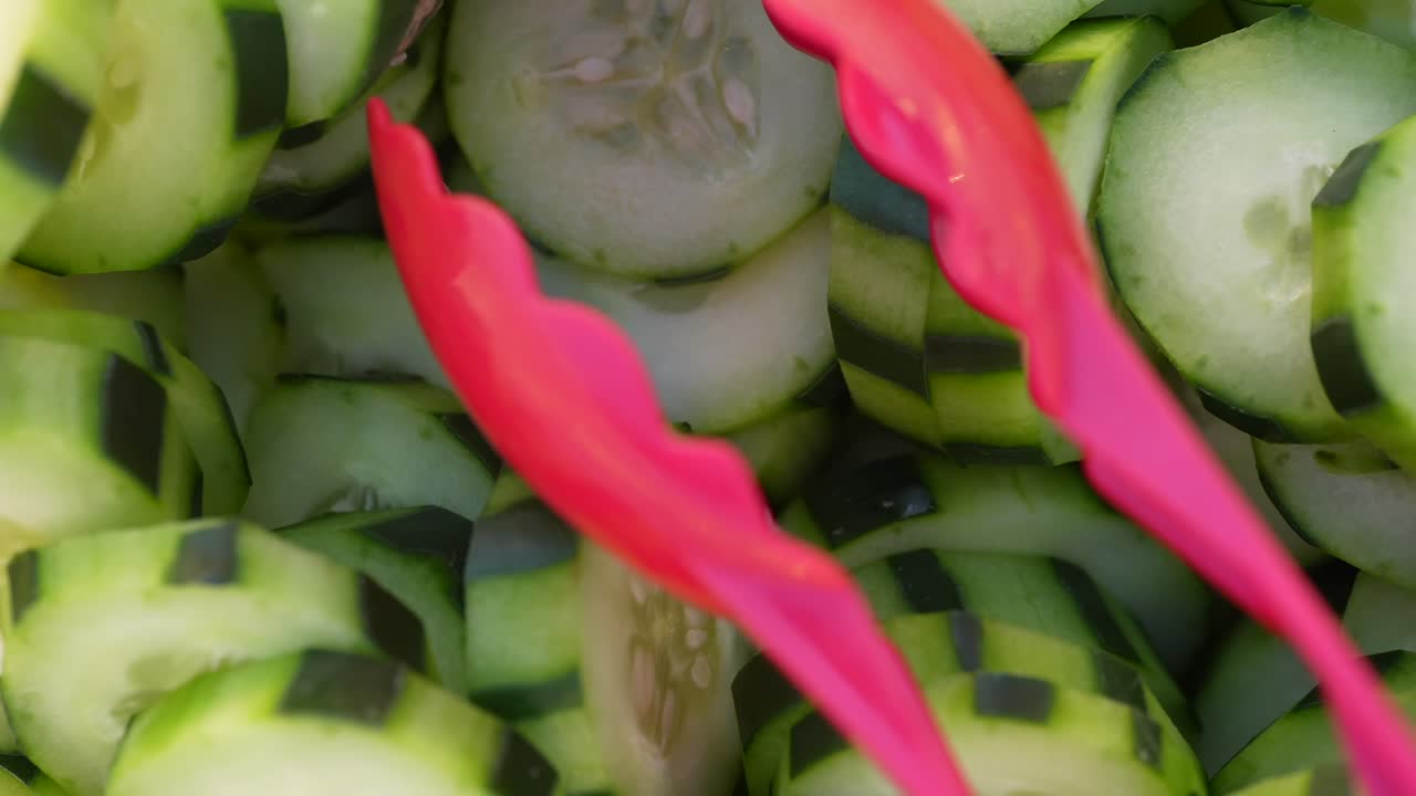 Primo piano dall'alto di fette di cetriolo verde prese con una pinza rossa, che evidenziano la freschezza, la consistenza croccante e verdure crude salutari.