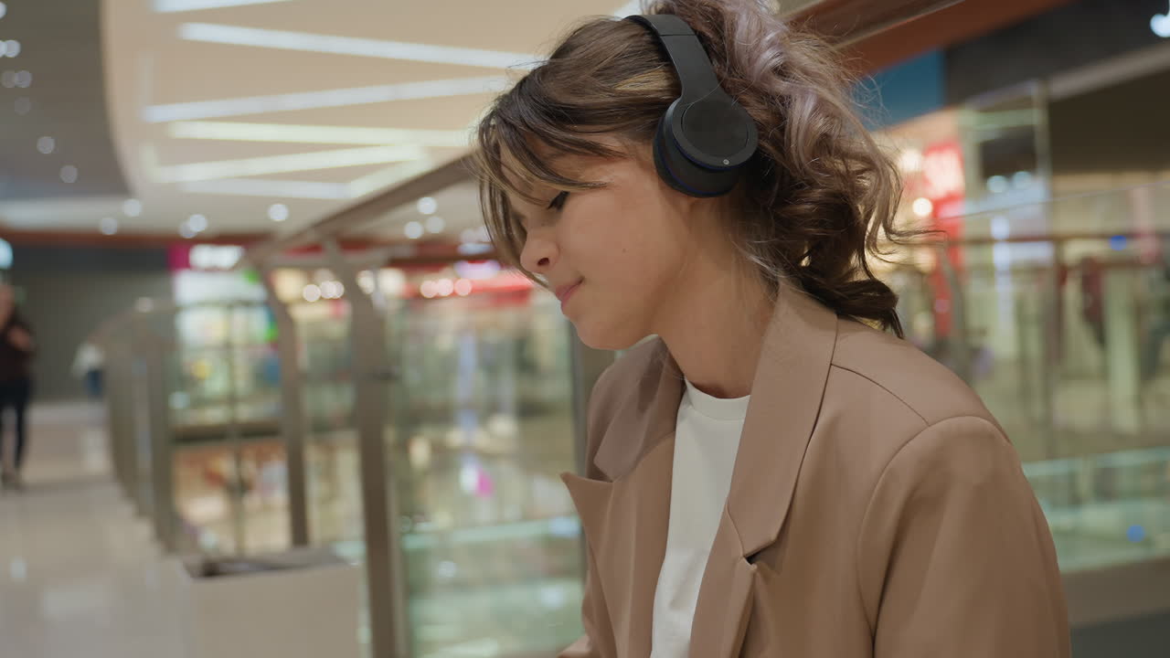 Mujer joven estudiando, chica moderna relajándose en una zona comercial, estudiante disfrutando de un momento de tranquilidad en un atrio luminoso, joven haciendo una pausa relajante en un centro comercial moderno