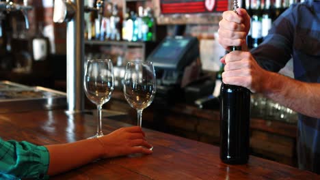 Barman-opening-wine-bottle-with-corkscrew-at-bar-counter