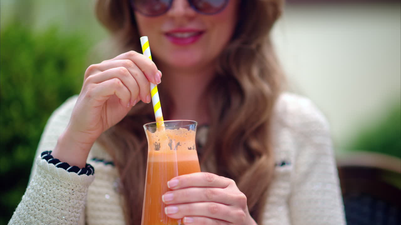 Woman drinking an orange juice using of a straw, at a cafe, outside