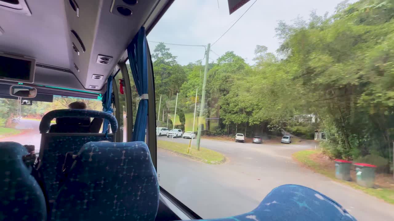 Passenger view inside moving bus, traveling through green rainforest road with natural daylight, steady camera