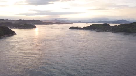 Ship-travels-under-bridge,-Tilt-up-Reveals-Seto-Inland-Sea-of-Japan-at-Sunset