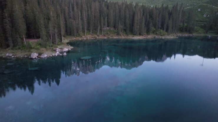 Frau mit Hut hebt die Arme und bewundert den Alpensee Karersee, Südtirol, Luftaufnahme