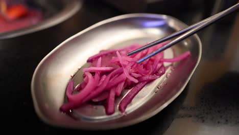 chopsticks picking up pickled red onions from dish