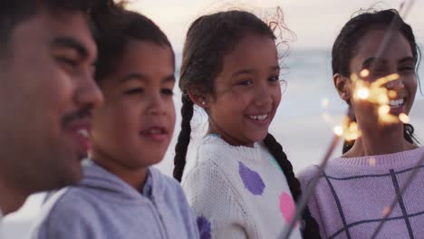 portrait of happy hispanic family playing with sparklers on beach at sunset