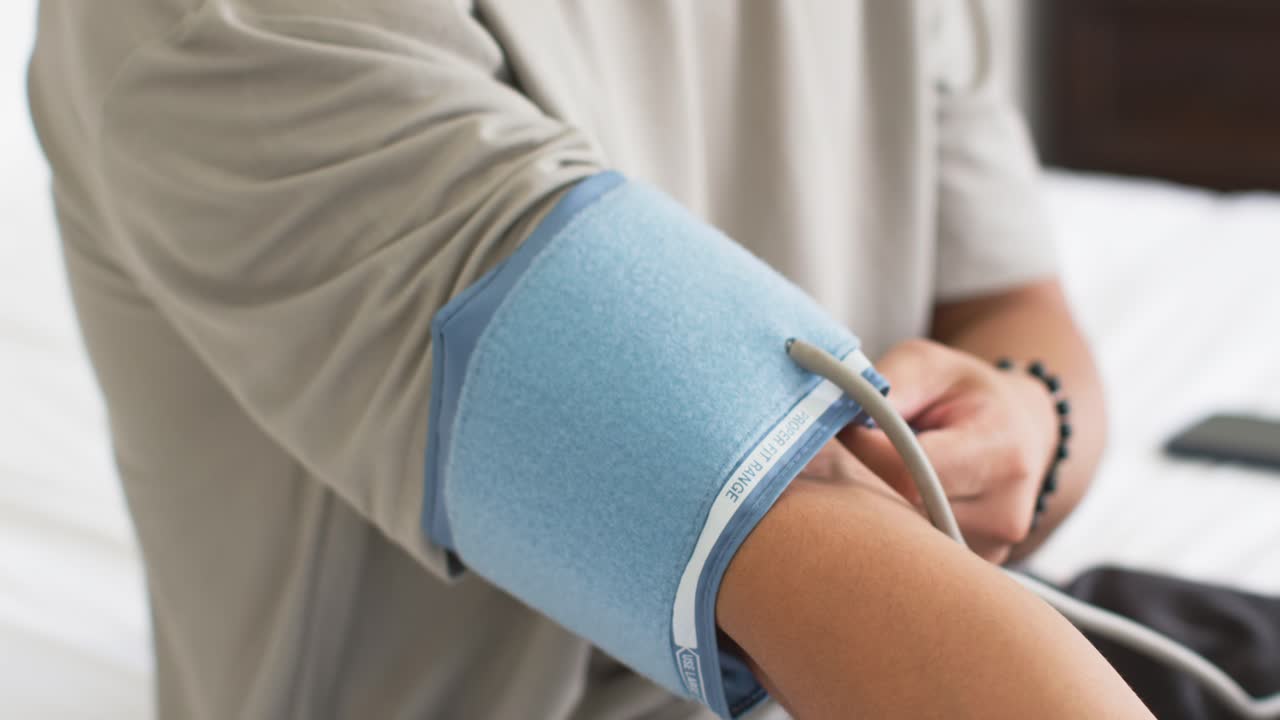 Uomo sul letto che inserisce il braccio sinistro in un bracciale blu, fissando il velcro e sistemando il tubicino per un controllo medico.