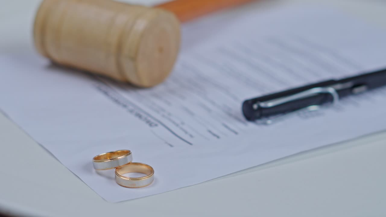 Two gold wedding rings on divorce decree papers with a wooden judge gavel and pen