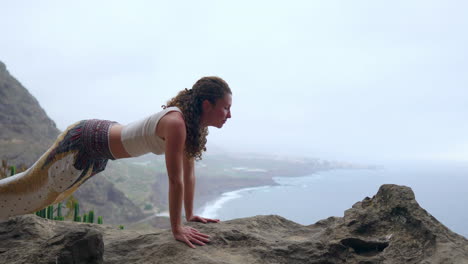 positioned on a cliff's edge, the woman practices a dog pose, overlooking the ocean, as she breathes in the sea air during her yoga journey across the islands