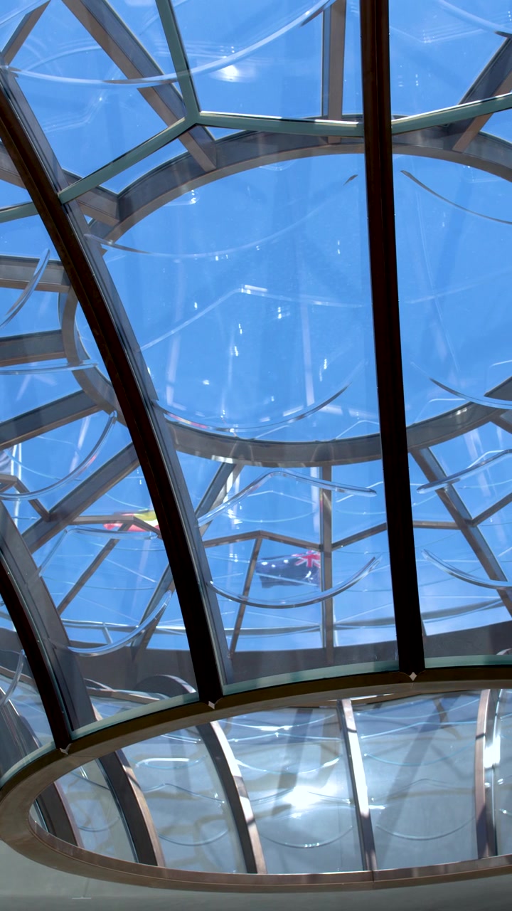 Inquadratura dal basso di una cupola geometrica in vetro sul soffitto contro un cielo azzurro e limpido.