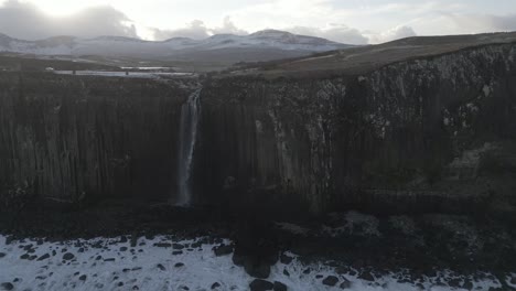 Majestic-Kilt-Rock-Waterfall-in-Scotland-with-snow-patches,-serene-landscape-under-cloudy-skies