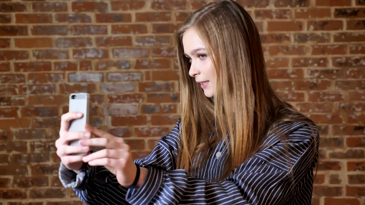 joven hermosa está haciendo video en su teléfono inteligente, hablando, concepto de comunicación, fondo de ladrillo