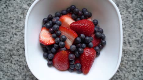 overhead view of sliced strawberries and blueberries on the white bowl