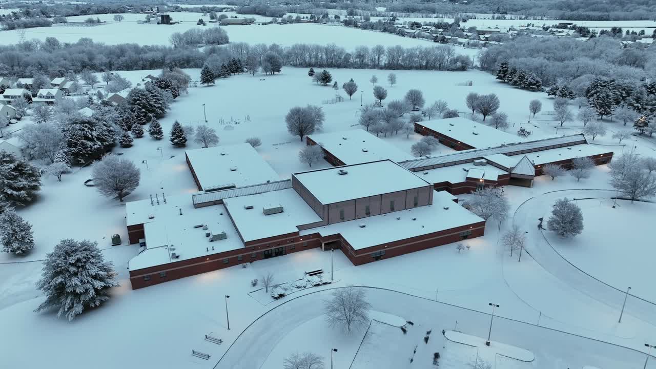 Luftfoto med drone af et sneklædt skoleområde i Lancaster, Pennsylvania i vintertusmørke. Stort bygningskompleks er omgivet af sneklædte marker, træer og et roligt forstadsmiljø