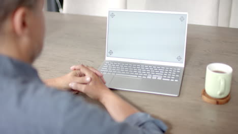 Senior-biracial-man-at-table-with-coffee-having-video-call-on-laptop,-copy-space-screen,-slow-motion