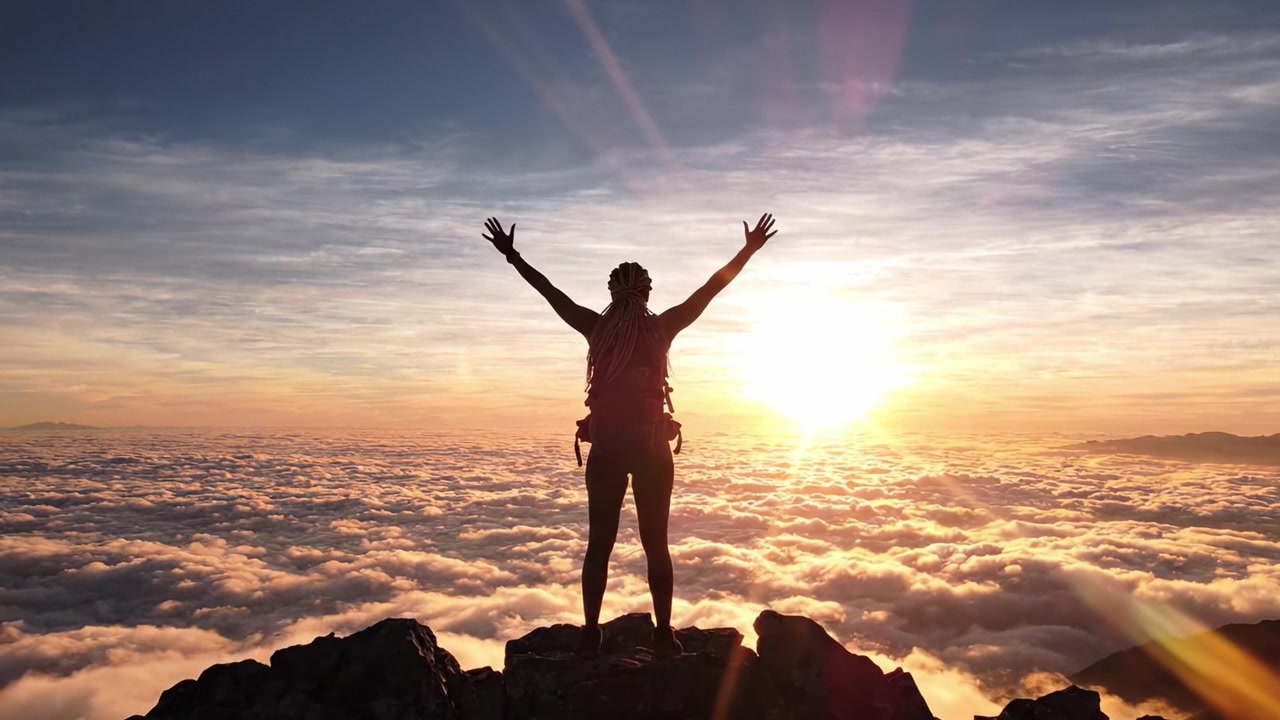 Escalador Eufórico Celebrando el Triunfo en la Cima de la Montaña Durante un Impresionante Amanecer Sobre las Nubes, Abrazando el Momento con los Brazos Extendidos y una Sensación de Logro y Libertad.
