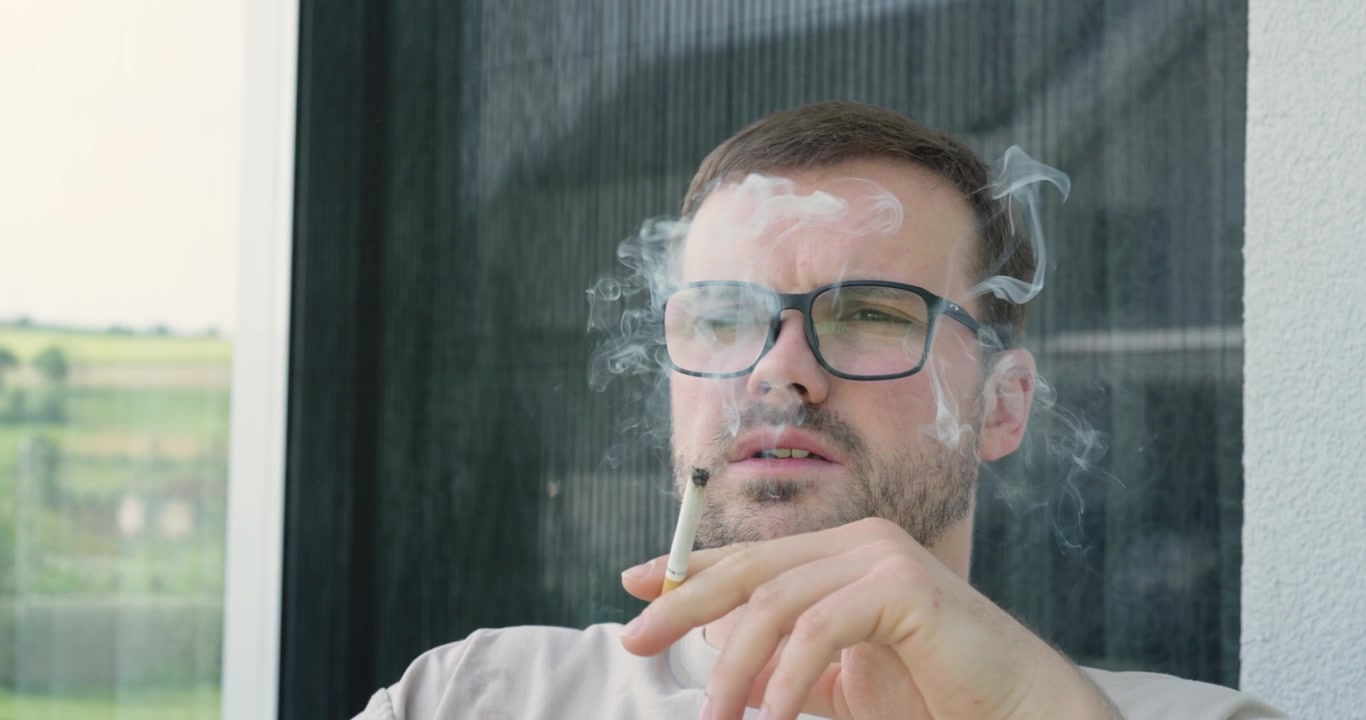 Hombre fumando un cigarrillo al aire libre con humo visible. Concepto de consumo de tabaco, adicción a la nicotina, estilo de vida poco saludable y hábitos de tabaquismo.