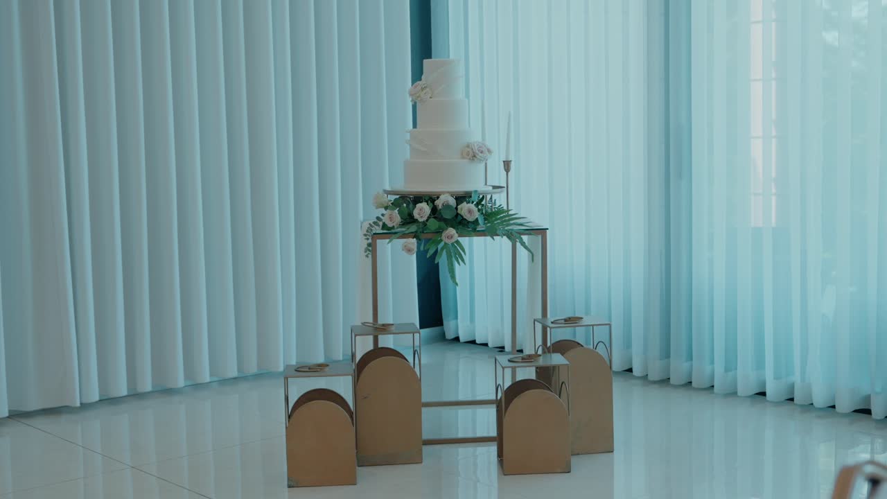 Wedding cake on a modern gold stand with floral decor in a light filled venue