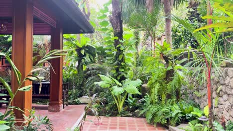 a serene view of lush tropical foliage surrounding a traditional thai teak house, captured in vibrant daylight