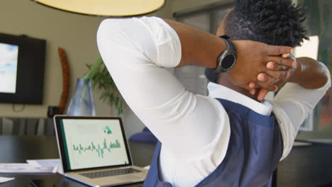 Rear-view-of-young-black-businessman-with-hands-behind-head-while-working-on-laptop-in-office-4k