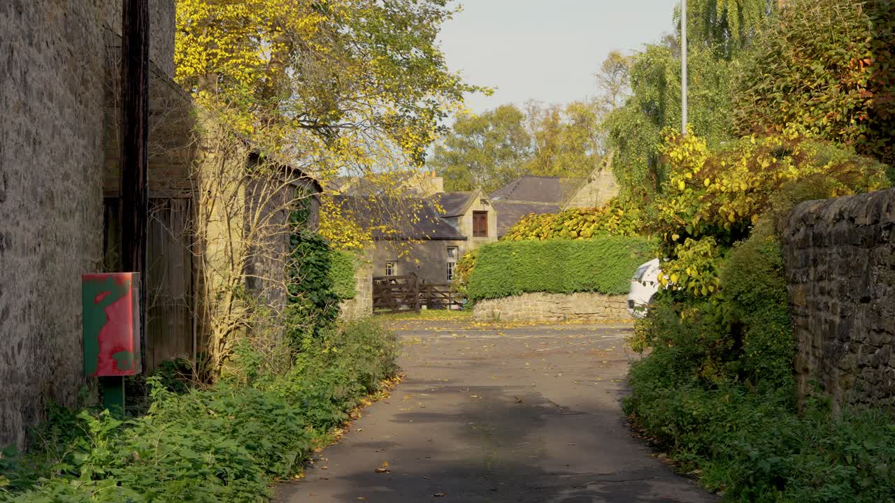 A white RV drives past a rural lane surrounded by stone walls and autumn foliage