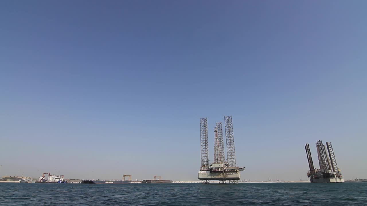 Bevægelig optagelse fra en båd af olierigge tæt på havn og tørdok, der afventer reparationer og genudstationering til søs i Bahrain i Den Arabiske Golf