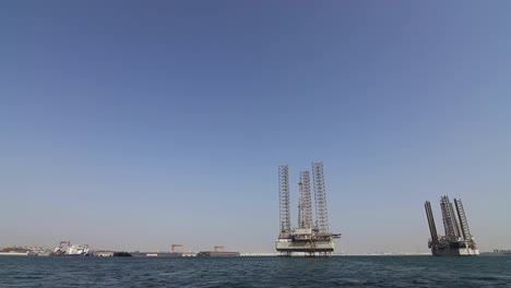 moving shot from a boat of oil rigs close to port and dry dock awaiting repairs and re-deployment at sea in bahrain in the arabian gulf.