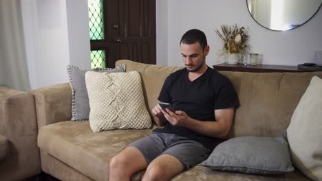 man sitting upright on couch using mobile phone