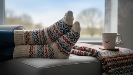cozy comfort in winter: a relaxing scene with warm socks, a hot beverage, and a knit blanket by the window on a chilly day
