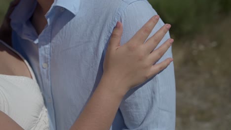 close up of woman's hand gently resting on a man's shoulder, both wearing light clothing, symbolizing affection and connection