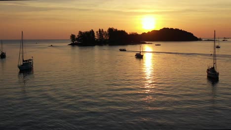 sailing sunset landscape view, aerial forward flying capturing glowing sun setting behind seratos island and paradise 101, reflection on calm sea ocean, tropical paradise at langkawi, kedah, malaysia