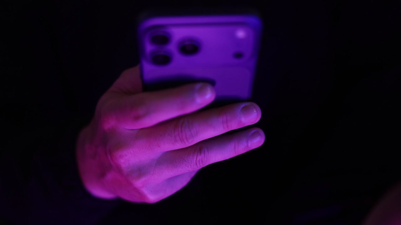 Ripresa ravvicinata dal retro di una persona che tiene uno smartphone con una mano e scorre i contenuti su un dispositivo mobile