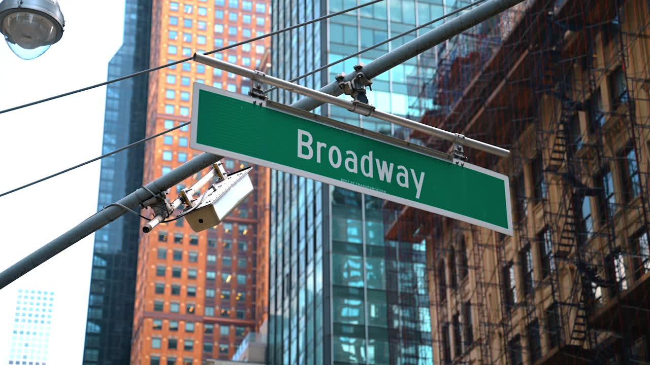 A green Broadway sign against tall modern buildings in New York City