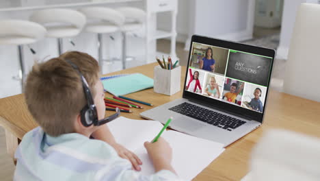 Schoolboy-using-laptop-for-online-lesson-at-home,-with-diverse-teacher-and-class-on-screen