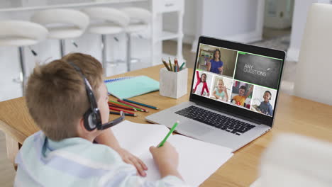 schoolboy using laptop for online lesson at home, with diverse teacher and class on screen