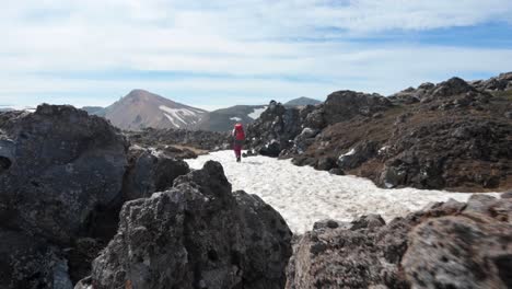 revelación de un excursionista caminando con una mochila en el parche de nieve entre rocas de magma negro en landmannalaugar en islandia