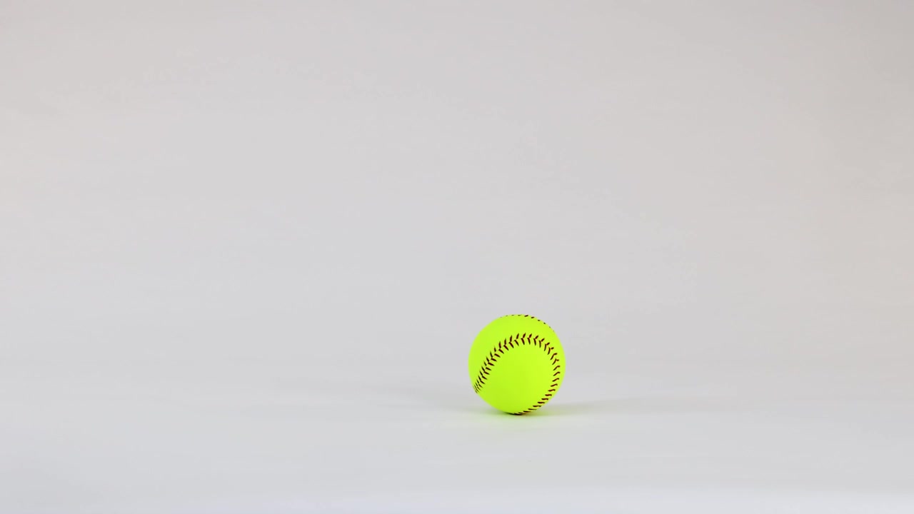 Palla da softball giallo neon che rimbalza e rotola su sfondo bianco