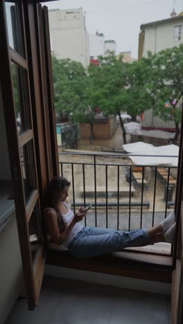 woman relaxing on balcony with smartphone on a rainy day