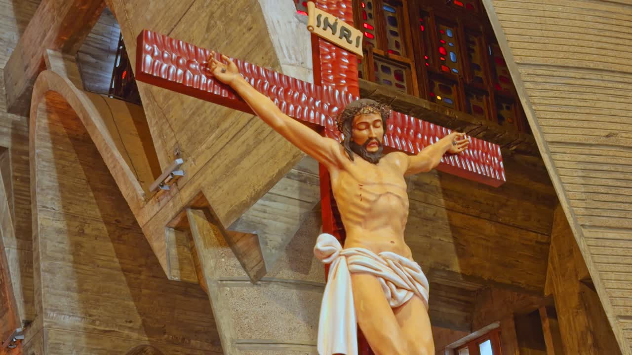 Dettagliato primo piano di un grande crocifisso in legno in stile moderno raffigurante Gesù Cristo sopra l'altare principale nella Basilica di Higüey, Repubblica Dominicana. Punto di vista dal basso.