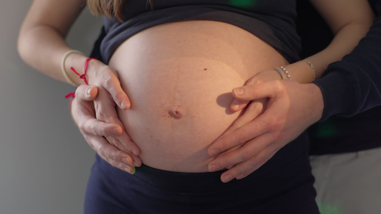 Mani della coppia che accarezzano la pancia della donna incinta con luci colorate