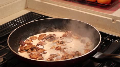 woman adding cream to sauted button mushrooms and stirring to make a light cream sauce