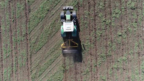 top down aerial view of a green fendt tractor pulling a heavy yellow cultivator and cultivating the compacted soil in a field to prepare it for the next crop.