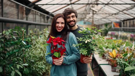 Beautiful-young-couple-in-casual-clothes-both-holding-plants,-looking-at-camera-and-smiling