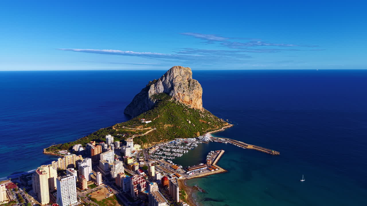 Costa di Calpe in Spagna con l'iconica formazione rocciosa del Peñón de Ifach che si erge dal Mar Mediterraneo accanto a un porto turistico e a edifici urbani sul lungomare